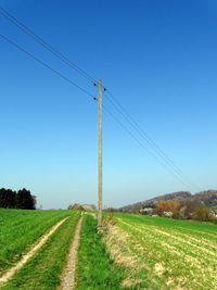 Electricity pylon on field against clear blue sky