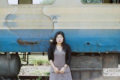 Portrait of young woman standing against abandoned train on railroad track