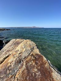 Rock formation in sea against clear blue sky