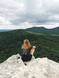 Rear view of woman sitting on cliff against landscape