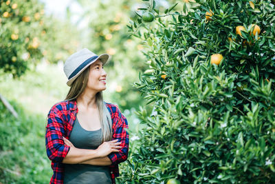 Smiling woman standing by orange tree in orchard