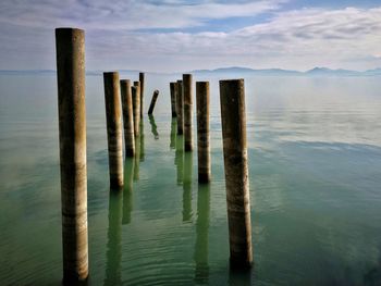 Wooden posts in lake against sky