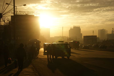 People and vehicles on street in city against cloudy sky during sunset