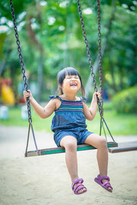 Full length of happy girl sitting on swing in playground