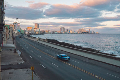 Road by buildings in city against sky during sunset