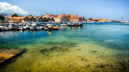 Sailboats moored in sea by town against sky