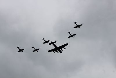 Low angle view of silhouette military airplanes flying against cloudy sky