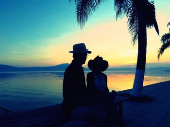 People looking at sea against sky during sunset