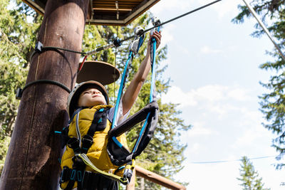 Low angle view of man hanging on rope against sky