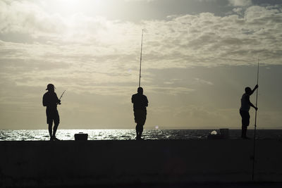 Silhouette people fishing at sea against sky