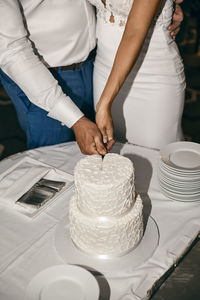 Midsection of couple cutting cake at wedding ceremony