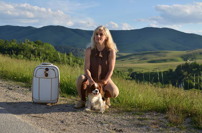 Woman and her dog, with suitcase in landscape in sunny afternoon