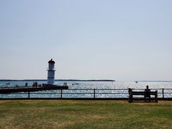 Lighthouse by sea against clear sky