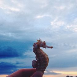 Low angle view of cropped hand against cloudy sky