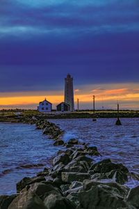 Lighthouse by sea against sky during sunset