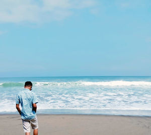 Rear view of man standing on beach against sky