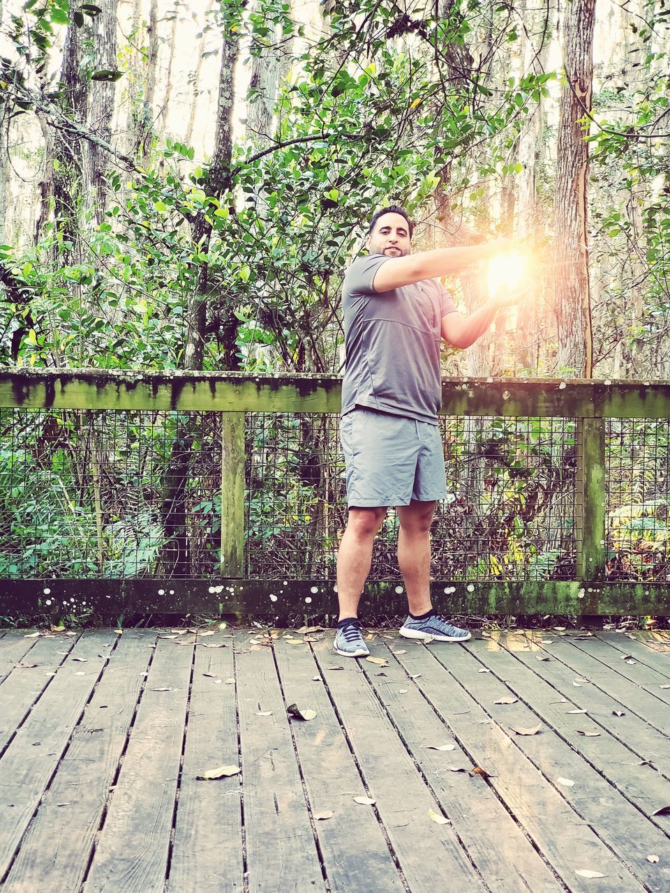 one person, full length, sunlight, casual clothing, nature, leisure activity, lifestyles, plant, standing, day, tree, lens flare, young adult, wood, adult, outdoors, outdoor structure, sunbeam, front view, women, men, backyard, walkway, architecture, footpath, growth, boardwalk, person, built structure, clothing