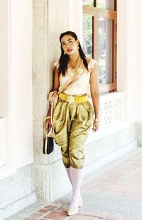 Portrait of young woman standing against wall at home