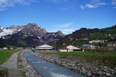 Road by river and buildings against blue sky