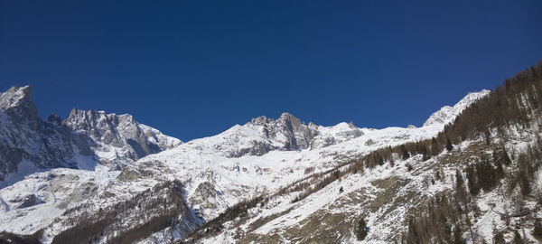 Low angle view of snowcapped mountains against clear blue sky