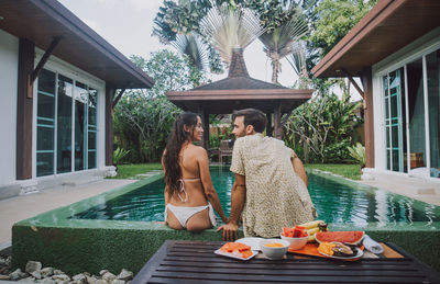 Rear view of couple sitting by swimming pool