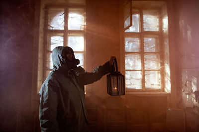 Woman holding oil lamp wearing gas mask standing amidst smoke