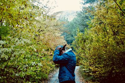 Side view of young man standing on footpath amidst trees and plants at autumn