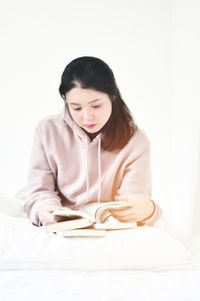 Beautiful young woman sitting on bed against white background