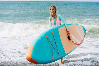 Young blonde woman holding stand up paddle board