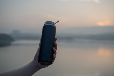 Midsection of woman holding umbrella against sea during sunset