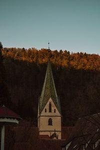 Cross amidst trees and buildings against sky