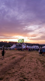 People walking on land against sky during sunset