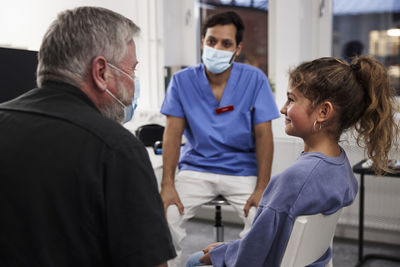 Male doctor talking to girl patient and grandfather during appointment