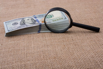 Close-up of magnifying glass and paper currencies on table
