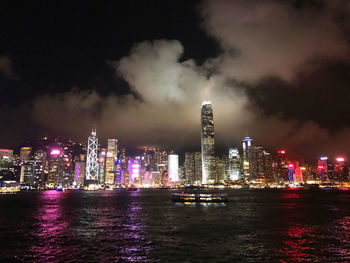Illuminated buildings by river against sky at night