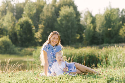 A young asian mom and a young son sitting on the grass near the lake spend a sunny day together 