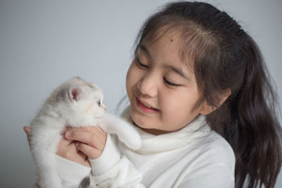 Girl playing with scottish fold cat while sitting against wall at home