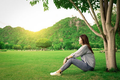 Woman sitting on grass against trees