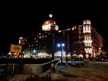 Illuminated buildings by street against sky at night