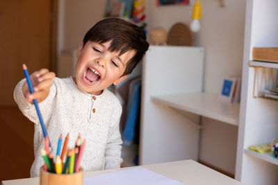 Happy boy holding colored pencil at home