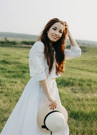 Portrait of smiling beautiful woman with sun hat standing on grassy land