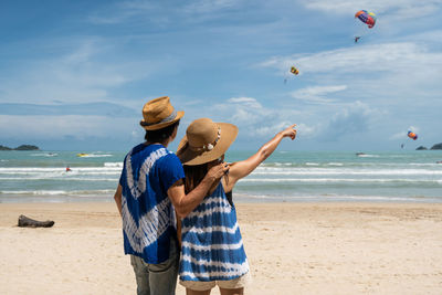 Rear view of friends standing on beach against sky