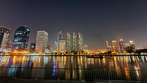 Illuminated buildings by river against sky in city at night
