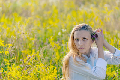 Portrait of young woman standing amidst flowering plants on field