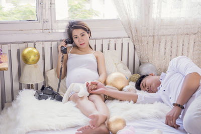 Portrait of pregnant woman talking on phone with boyfriend sleeping on bed at home