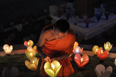 Rear view of man sitting on illuminated candles