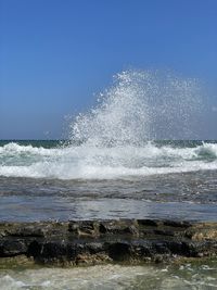 Sea waves splashing on shore against clear sky