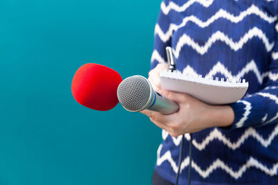 Close-up of woman holding microphone and note pad against colored background