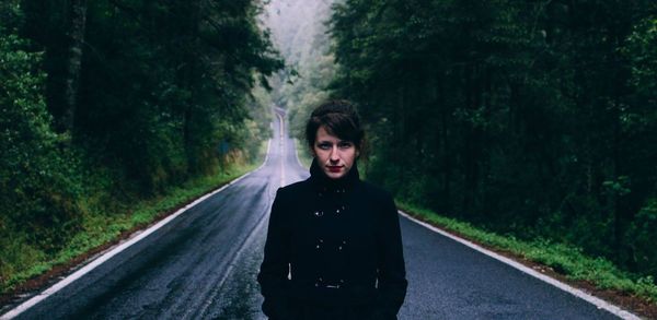 Portrait of young woman standing on road in forest