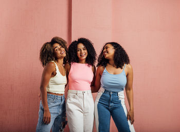 Portrait of young female friends standing against wall